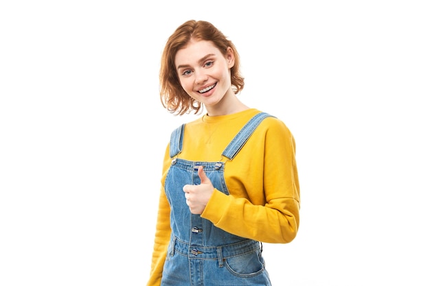 Young redhead woman shows hand with thumbs up and smiles at the camera isolated on white background