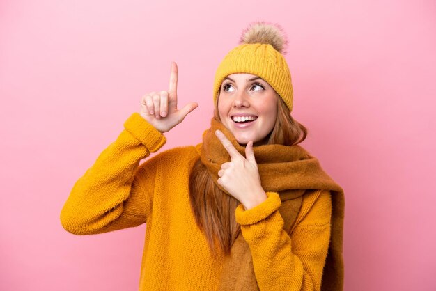 Young redhead woman wearing winter jacket isolated on pink background pointing with the index finger a great idea