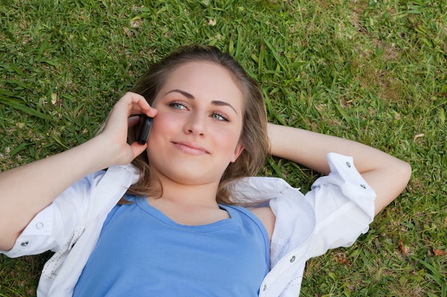 Young relaxed blonde girl lying on her back while talking on the phone