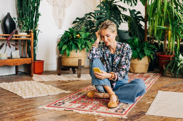 Young relaxed blonde woman sitting on the floor uses phone for online communication