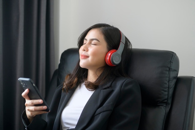 Young relaxing business woman using smartphone and listening to music in modern office