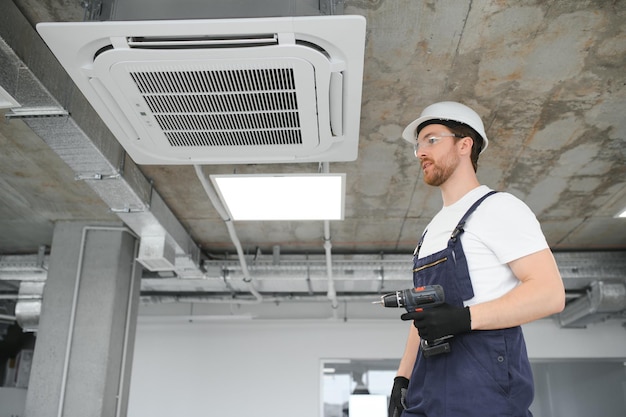 Young repairman repairing ceiling air conditioning unit