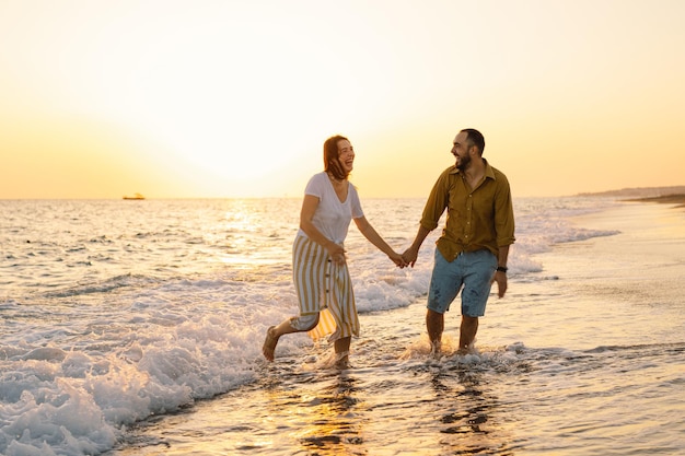 Young romantic couple dancing turning around by sea Seascape at sunset with beautiful sky Romantic couple on the beach at golden sunset Lover couple having fun on beach