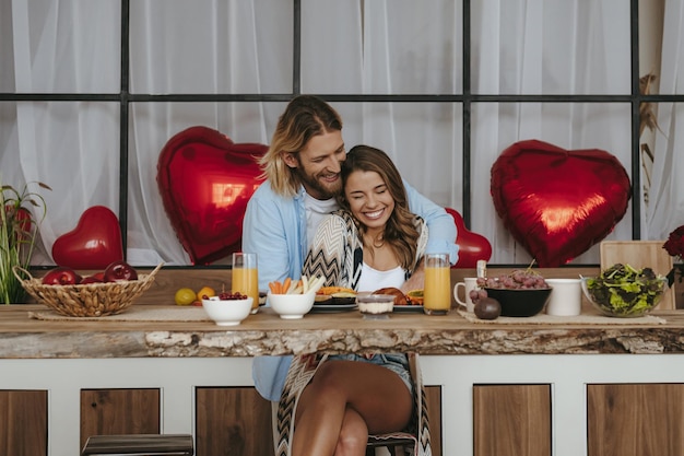 Young romantic couple embracing while celebrating Valentines day with red balloons on background