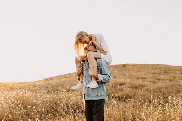 Young romantic couple in a field. Man holding woman on his shoulders.