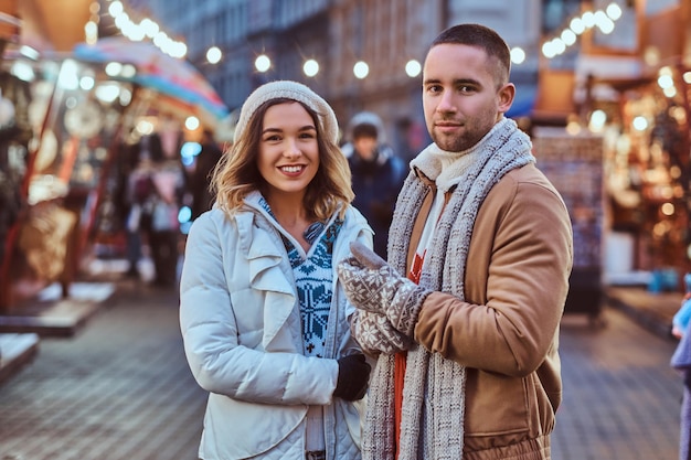 A young romantic couple walking on the street at Christmas time, standing near decorated shops in the evening