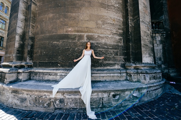 Young romantic elegant girl in long white dress posing over stone ancient wall