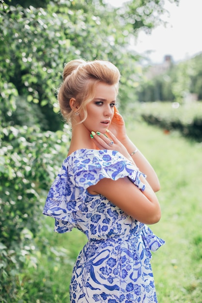 Young romantic woman in blue flower dress with makeup and hairstyle in green summer garden