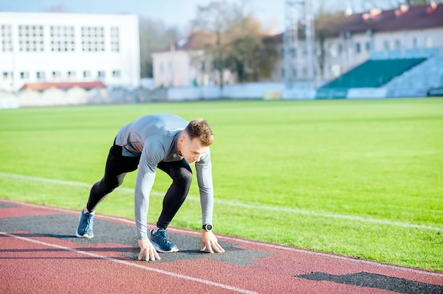 Young runner man in starting position ready for running on the stadium racetrack.