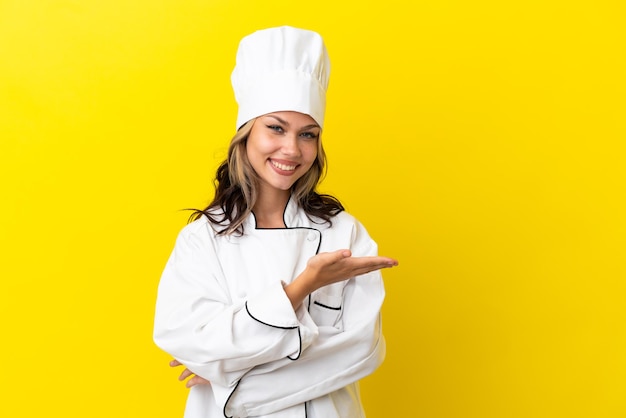 Young Russian chef girl isolated on yellow background presenting an idea while looking smiling towards