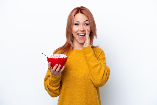 Young Russian girl holding a bowl of cereales isolated on white background shouting with mouth wide open