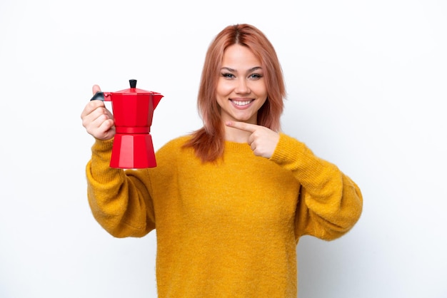 Young Russian girl holding coffee pot isolated on white background and pointing it