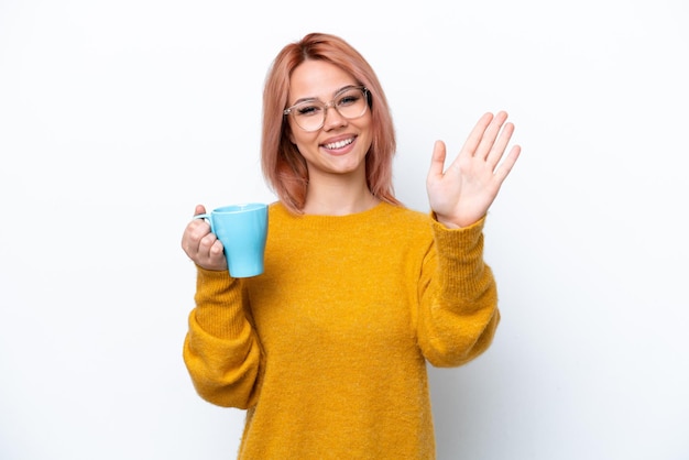 Young Russian girl holding cup of coffee isolated on white background saluting with hand with happy expression