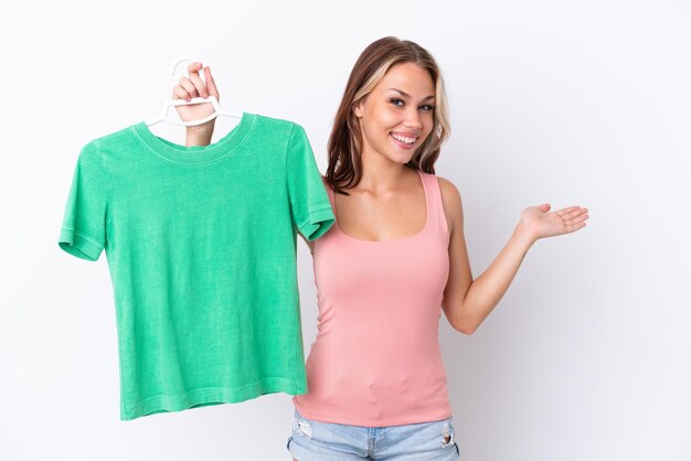 Young Russian girl holding hanger isolated on white background extending hands to the side for inviting to come