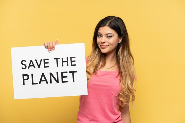 Young Russian girl isolated on yellow background holding a placard with text Save the Planet