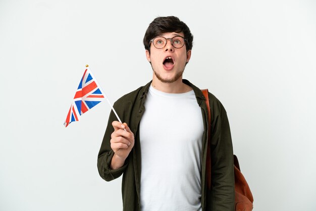 Young Russian man holding an United Kingdom flag isolated on white background looking up and with surprised expression