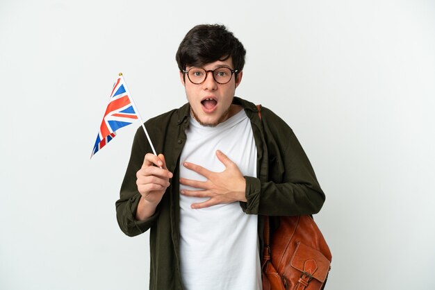 Young Russian man holding an United Kingdom flag isolated on white background surprised and shocked while looking right