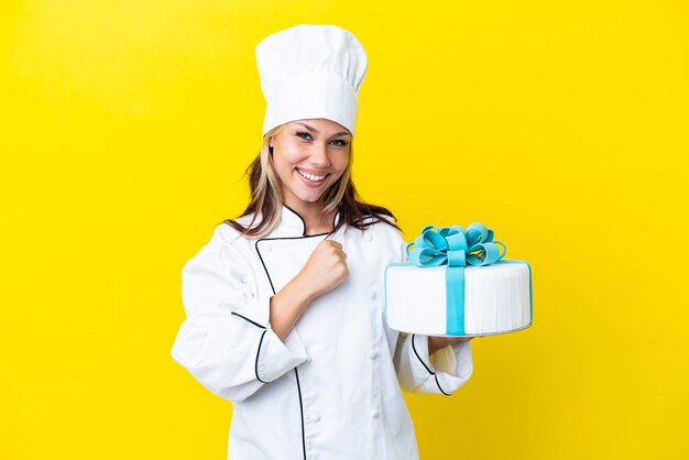 Young Russian pastry chef woman with a big cake isolated on yellow background celebrating a victory