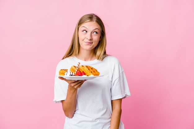 Young russian woman eating a waffle isolated dreaming of achieving goals and purposes