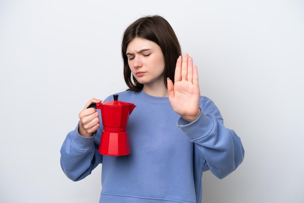 Young Russian woman holding coffee pot isolated on white background making stop gesture and disappointed