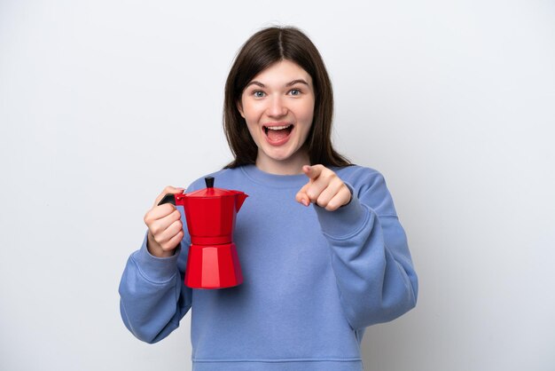 Young Russian woman holding coffee pot isolated on white background surprised and pointing front