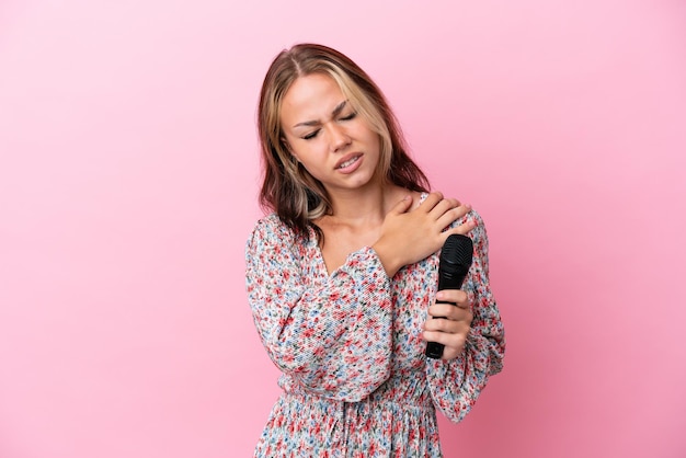 Young Russian woman holding a microphone isolated on pink background suffering from pain in shoulder for having made an effort