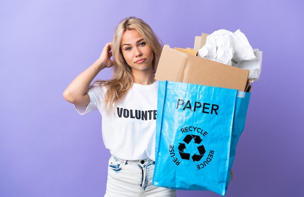 Young Russian woman holding a recycling bag full of paper to recycle isolated on purple background having doubts