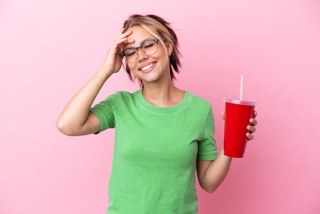 Young Russian woman holding a refreshment isolated on pink background smiling a lot