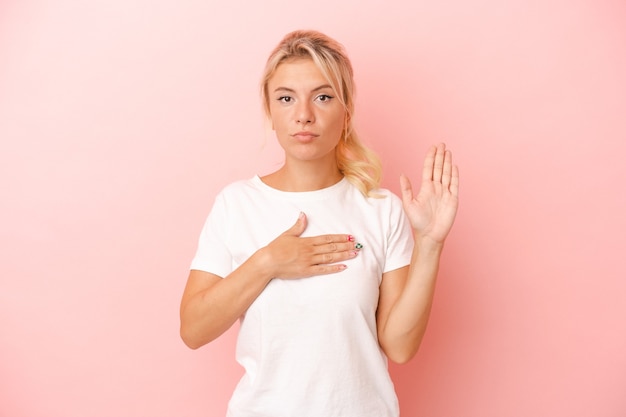 Young Russian woman isolated on pink background taking an oath, putting hand on chest.