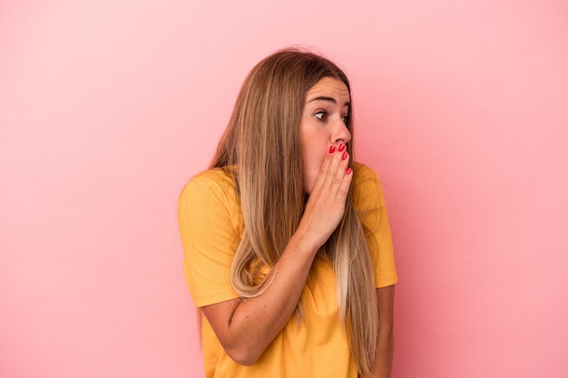 Young Russian woman isolated on pink background thoughtful looking to a copy space covering mouth with hand.