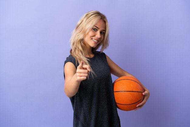 Young Russian woman isolated on purple playing basketball and pointing to the front