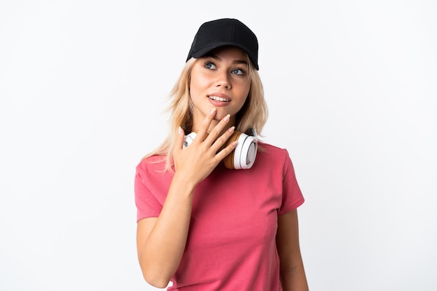 Young Russian woman listening music isolated on white looking up while smiling