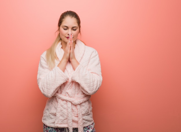 Young russian woman wearing pajama praying very happy and confident