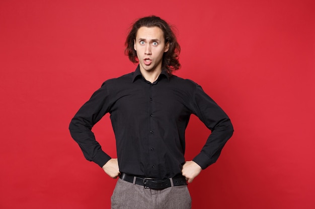 Young sad curly long haired man in black shirt standing posing isolated on red wall background studio portrait. People sincere emotions lifestyle concept. Mock up copy space. Problem crisis depression