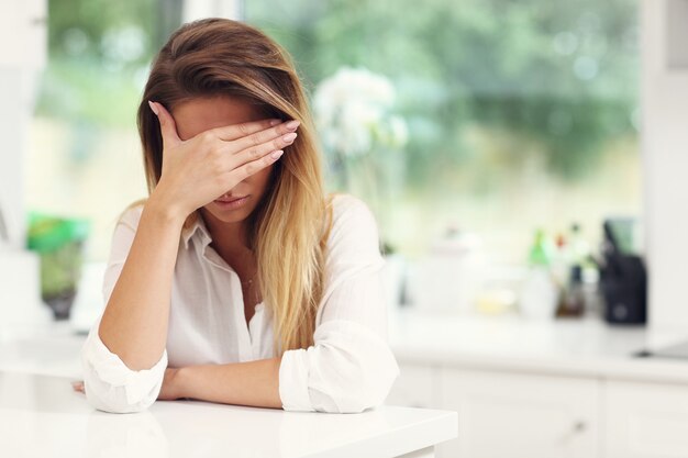 Young sad woman suffering from headache in kitchen