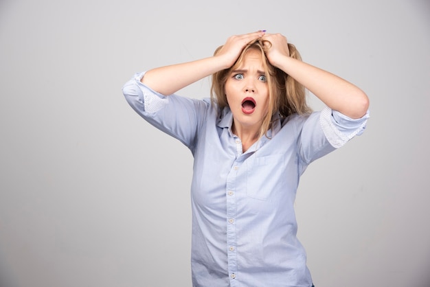 Young scared blonde woman with opened mouth holding hands on head.