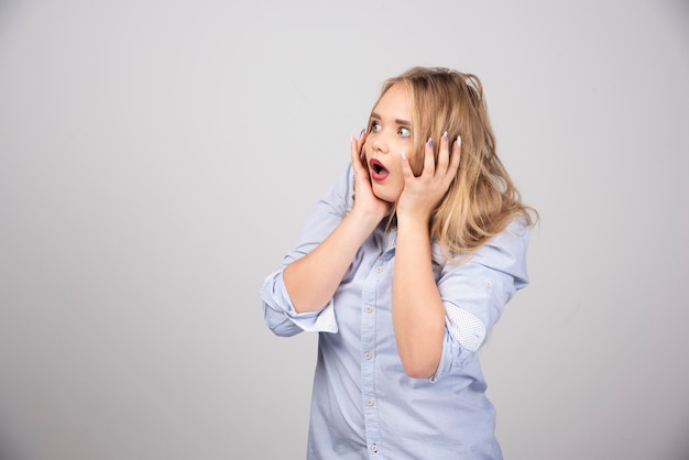 Young scared blonde woman with opened mouth holding hands on head.