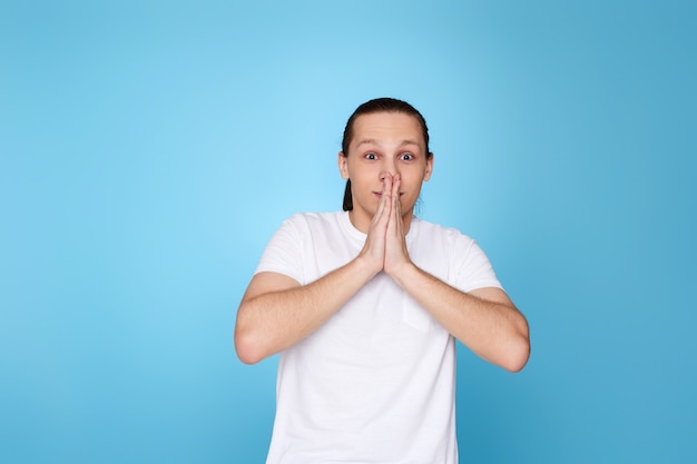 Young scared man in t-shirt isolated on blue background.