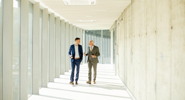 Young and a senior businessman walk down an office hallway deep in conversation