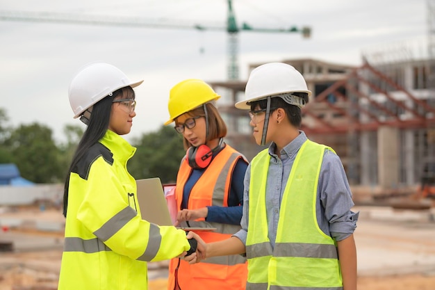 Young and senior Engineers discuss about work of large building underconstructionThree people working on site of under construction