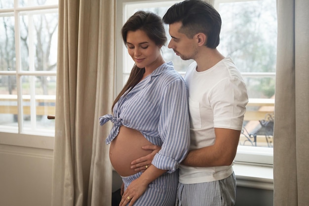 Young sensual couple are waiting for a baby Man and his pregnant wife in embrace beside the window