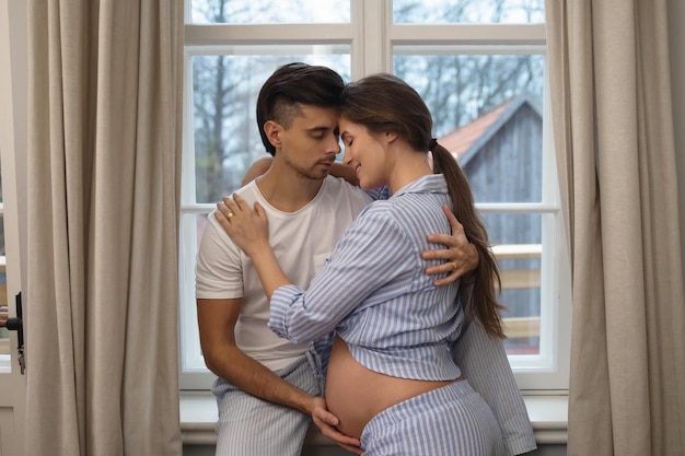 Young sensual couple are waiting for a baby Man and his pregnant wife in embrace beside the window