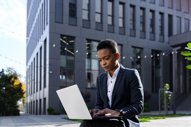 Young serious african american woman studying online sitting remotely in the park businesswoman working on laptop pensive and focused