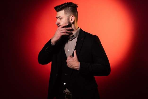 Young serious bearded man in black suit on red background