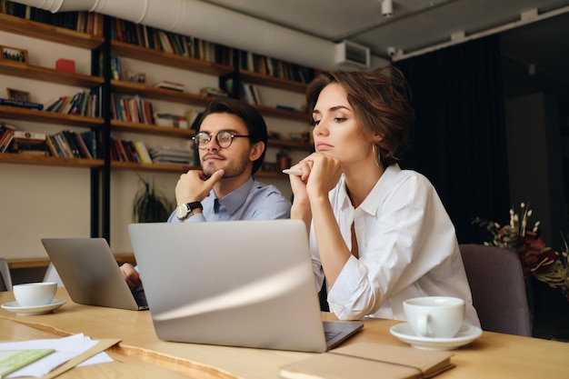 Young serious business colleagues thoughtfully working on new project with laptop and coffee in modern office