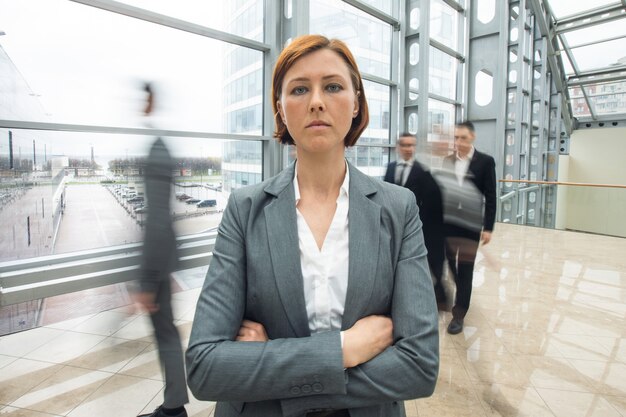 Young serious redhead businesswoman standing in a crowd with arms crossed