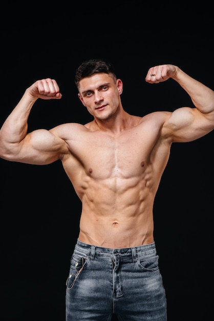 A young sexy athlete with perfect abs poses in the studio topless in jeans on the background. Healthy lifestyle, proper nutrition, training programs and nutrition for weight loss.