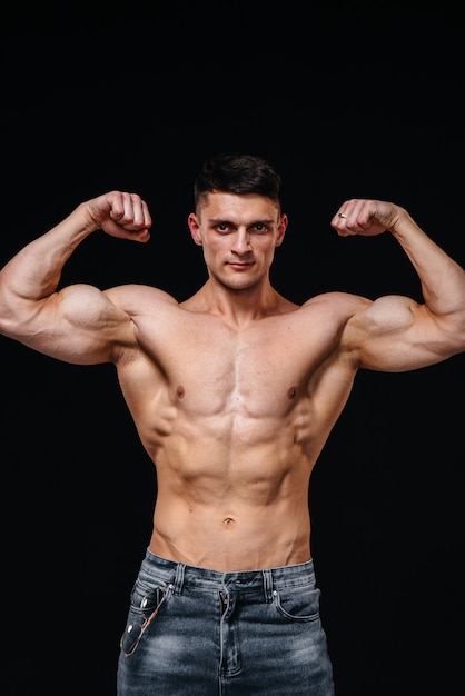 A young sexy athlete with perfect abs poses in the studio topless in jeans