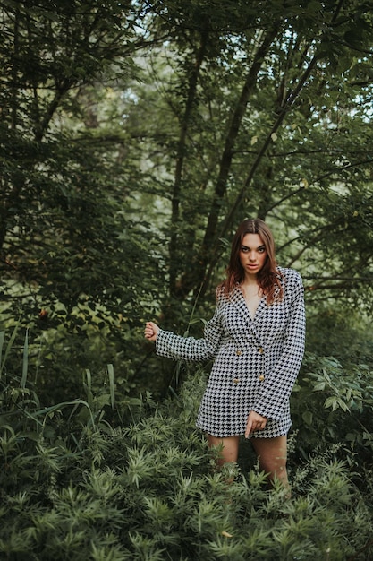 Photo young sexy brunette girl with a resting face posing in a green forest in a trendy outfit