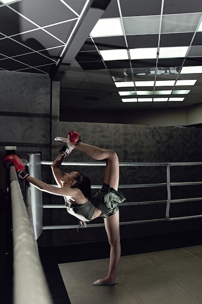 Young sexy girl in boxing gloves and sportswear doing stretching in the ring